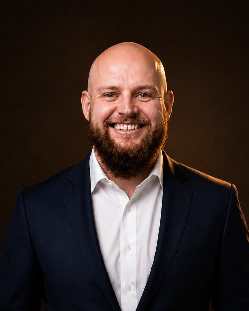 Erik Mollen, photographed against a dark ground in a navy suit.